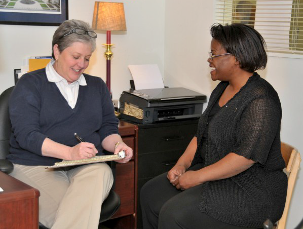 Two women sitting in an office. One is writing on a notepad. Counseling session.