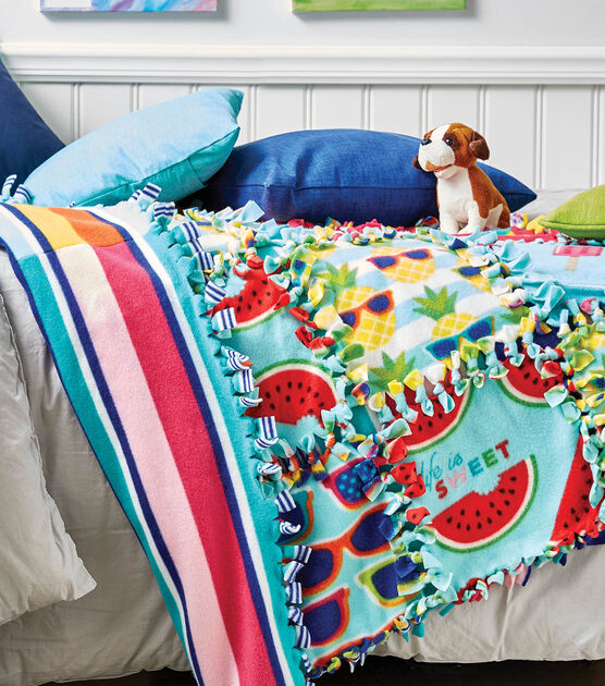 Colorful no-sew quilt laying on white bed. A teal and blue pillow are on top of the quilt.